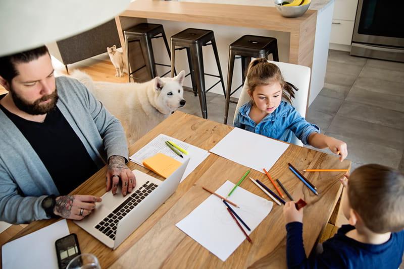 父亲在厨房用笔记本电脑，而孩子们画狗