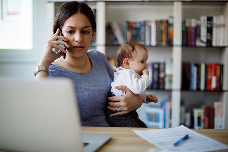 忙碌的工作妈妈拿着手机和笔记本电脑抱着宝宝